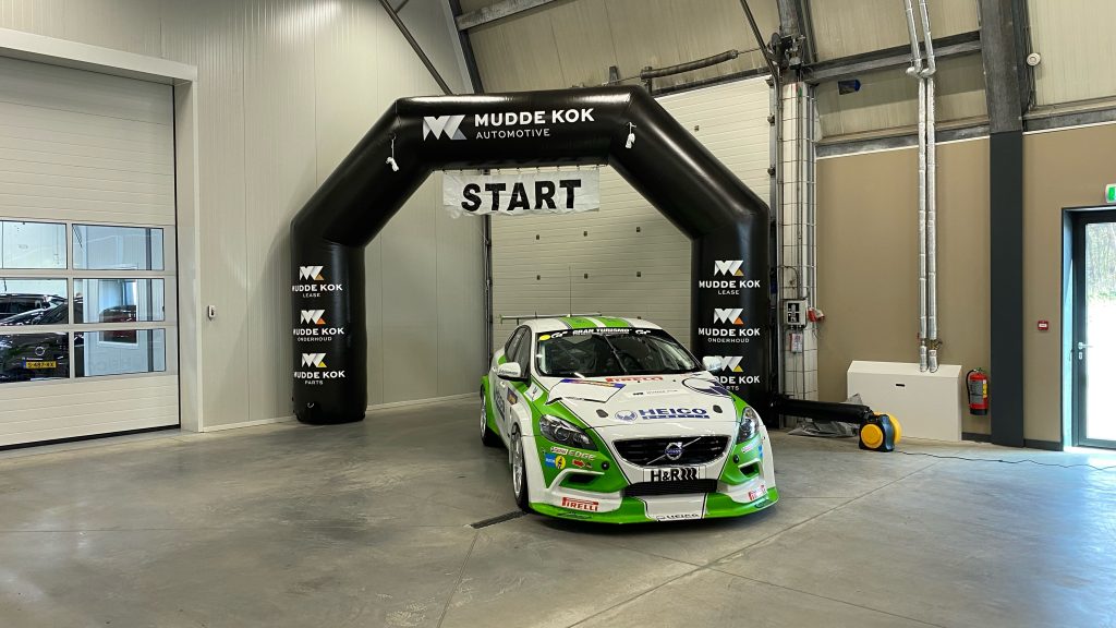 Zwarte opblaasbare boog met de tekst START in een bedrijfshal, met een raceauto eronder