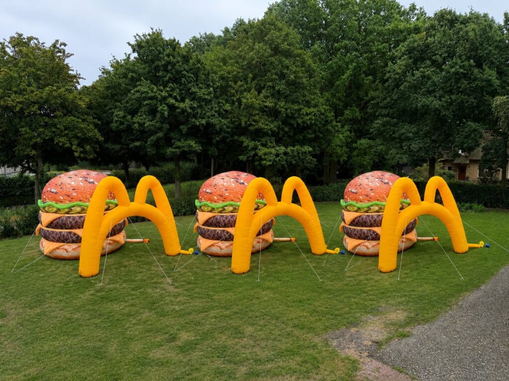 Drie opblaasbare hamburgervergrotingen met gele bogen op een grasveld