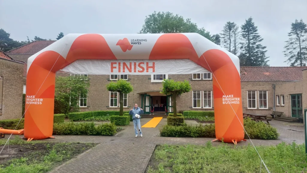 Oranje-witte opblaasbare boog met de tekst FINISH boven het pad naar de ingang van een bakstenen gebouw